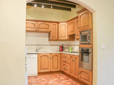 A kitchen with wooden cabinets a dishwasher a sink an oven and a microwave at Stoney Cottage in Narberth Pembrokeshire