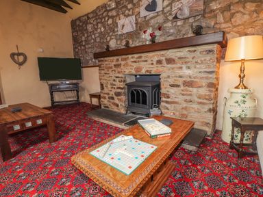 A living room with a stone fireplace a wood stove a coffee table with Scrabble game and a television at Stoney Cottage Narberth Pembrokeshire