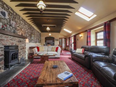 A living room with stone fireplace wooden tables sofas and red patterned carpet at Stoney Cottage Narberth Pembrokeshire