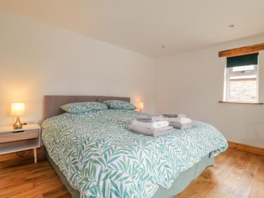 A bedroom with a double bed with green leaf patterned bedding two bedside tables with lamps and a window at Stoney Cottage in Narberth Pembrokeshire