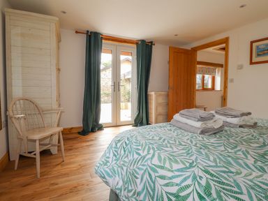 A bedroom with a bed covered in patterned bedding and folded towels a wooden chair a cabinet and a chest of drawers at Stoney Cottage Narberth Pembrokeshire