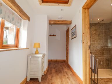 A hallway with wooden floors and beams a small white chest with a yellow lamp and a bathroom with tiled walls visible at Stoney Cottage in Narberth Pembrokeshire