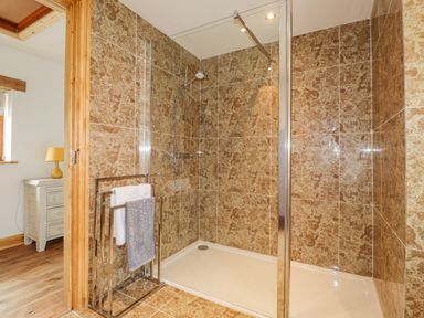 A shower area with tiled walls and a glass door next to a towel rack with towels at Stoney Cottage in Narberth Pembrokeshire