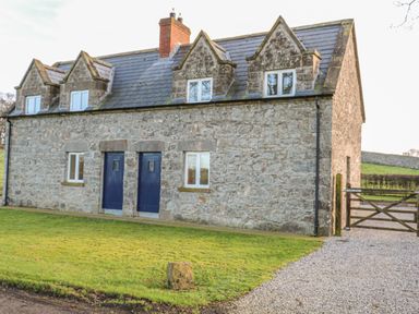 A stone cottage with blue doors and windows and a gravel driveway with a wooden gate at Goose Cottage in Caledon near Killylea