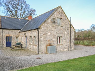 A stone cottage with a slate roof a blue door picnic table and gravel driveway at Goose Cottage in Caledon near Killylea