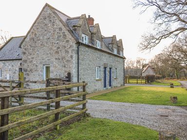 A stone house with a slate roof and wooden fence around a gravel driveway and grass at Goose Cottage Caledon near Killylea