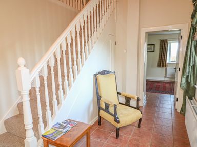 A hallway with a wooden chair and small wooden table near a carpeted staircase at Goose Cottage in Caledon near Killylea