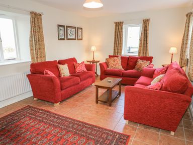 A living room with three red sofas a wooden coffee table two table lamps three framed botanical prints and patterned curtains at Goose Cottage in Caledon near Killylea