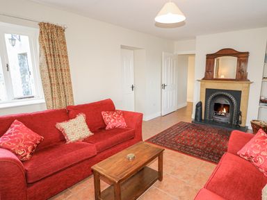 A living room with two red sofas a wooden coffee table a fireplace and patterned curtains at Goose Cottage in Caledon near Killylea