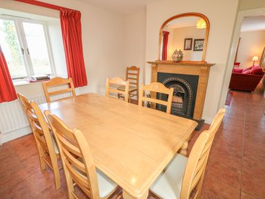 A dining room with a wooden table and chairs a window with red curtains and a fireplace with a mirror at Goose Cottage Caledon near Killylea