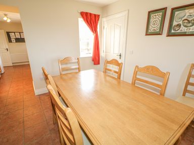 A dining room with a wooden table and six matching chairs next to a window with a red curtain and framed pictures on the wall at Goose Cottage in Caledon near Killylea