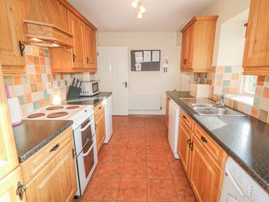 A kitchen with wooden cabinets a stove a microwave a sink and tiled floor at Goose Cottage Caledon near Killylea