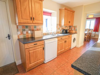 A kitchen with wooden cabinets dishwasher washing machine and tiled floor at Goose Cottage in Caledon near Killylea