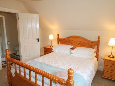 A bedroom with a wooden bed and bedside tables with lamps and an open door showing a bathroom at Goose Cottage in Caledon near Killylea