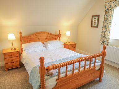 A bedroom with a wooden double bed white bedding two bedside tables with lamps a framed picture and a window with patterned curtains at Goose Cottage Caledon near Killylea