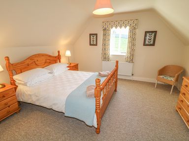 A bedroom with a wooden double bed bedside tables lamps window and a wicker chair at Goose Cottage in Caledon near Killylea