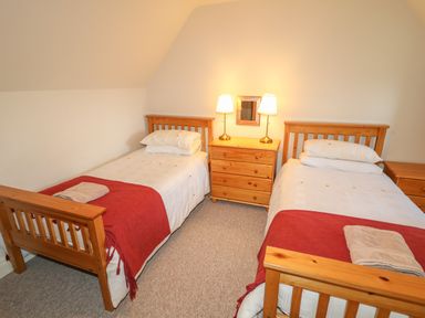 A bedroom with two single beds with wooden frames a wooden chest of drawers with two lamps and a small mirror at Goose Cottage in Caledon near Killylea