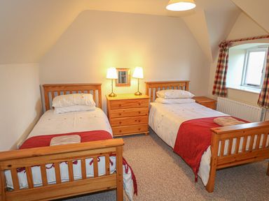 A bedroom with two single wooden beds a wooden chest of drawers with two lamps and a small window with curtains at Goose Cottage in Caledon near Killylea