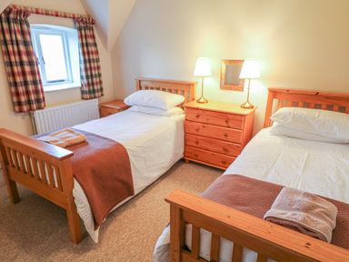 A bedroom with two single wooden beds a wooden chest of drawers with two lamps and a window with checked curtains at Goose Cottage in Caledon near Killylea