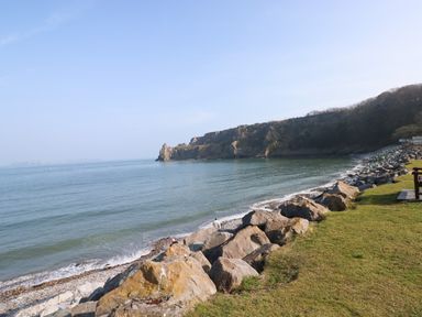 A rocky shoreline with grass and a wooden bench beside a calm sea at Smugglers in Lydstep