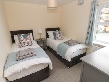 A bedroom with two single beds a nightstand lamp and a window with curtains at Smugglers in Lydstep