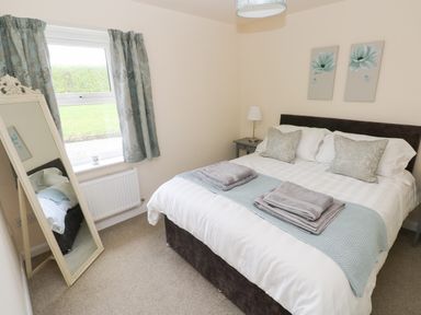 A bedroom with a bed folded towels bedside tables a lamp a window with curtains and a standing mirror at Smugglers in Lydstep