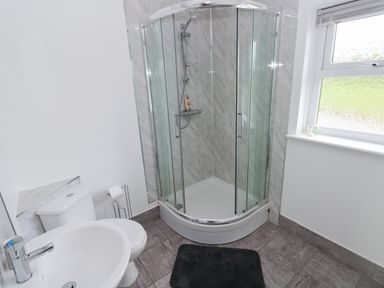 A bathroom with a shower enclosure a toilet a sink and a window at Smugglers in Lydstep