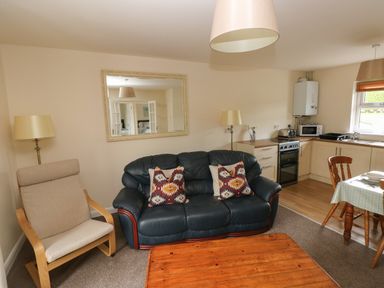 A living room with a black leather sofa with patterned cushions a beige armchair a wooden coffee table and a kitchen area with a dining table at Smugglers in Lydstep