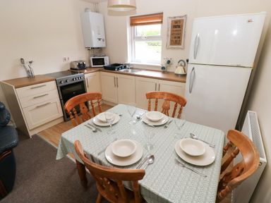 A kitchen with a dining table set for four with plates glasses and cutlery and kitchen appliances including a refrigerator oven microwave kettle and toaster at Smugglers in Lydstep