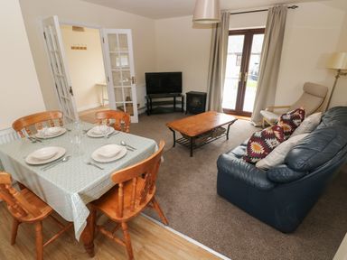 A dining area with a table set for four and a living room with a blue sofa, armchair, coffee table, and television at Smugglers in Lydstep