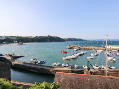A harbor with boats docked near a stone pier and a coastline in the background at Smugglers in Lydstep