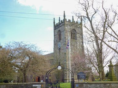 A stone church with a clock tower and a gate at Church Lane with trees and a flag in Gargrave