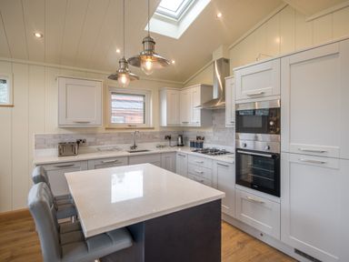 A kitchen with an island, two chairs, built-in oven, microwave, gas stove, and pendant lights at Wren Lodge in Gargrave