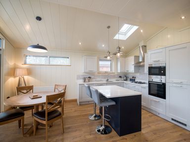 A kitchen with a dining table and chairs an island with stools and built in appliances at Wren Lodge in Gargrave
