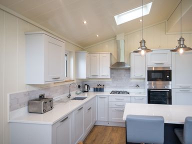 A kitchen with white cabinets a toaster microwave oven stove and island with chairs at Wren Lodge in Gargrave