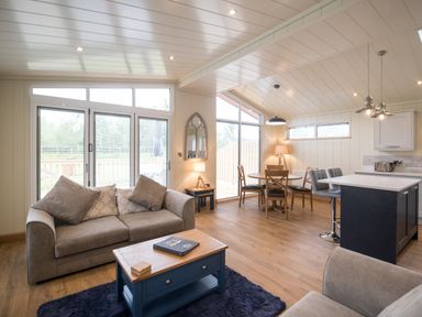 An open living area with a sofa coffee table dining table chairs bar stools and kitchen island at Wren Lodge in Gargrave