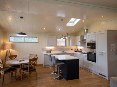 A kitchen with a dining table with four chairs and a kitchen island with two stools at Wren Lodge in Gargrave