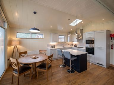 A kitchen and dining area with a round wooden table and chairs plus an island with stools at Wren Lodge in Gargrave