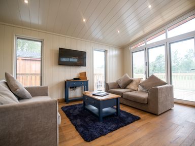 A living room with two sofas a coffee table and a TV on the wall at Wren Lodge in Gargrave