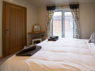 A bedroom with a wooden door a bed with folded towels and a window with curtains at Wren Lodge in Gargrave