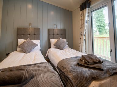 A bedroom with two single beds near a window with gray headboards and folded towels at Wren Lodge in Gargrave