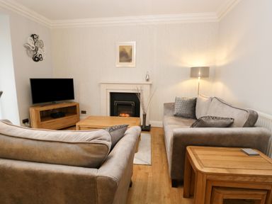 A living room with two sofas a wooden coffee table a fireplace and a television at Tethera in Bowness-On-Windermere
