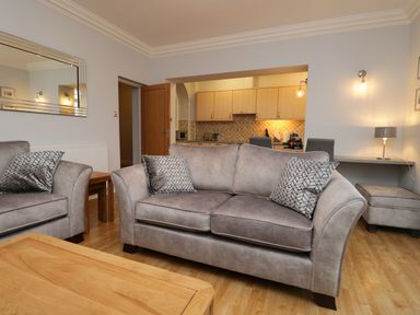 A living room with gray sofas and patterned cushions wooden coffee table and an open kitchen at Tethera in Bowness-On-Windermere