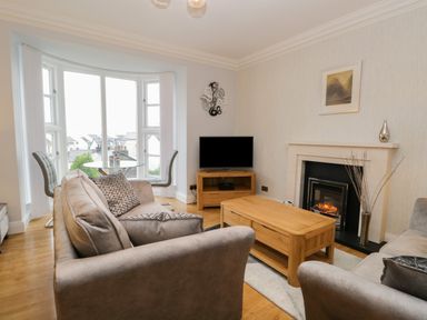 A living room with two gray sofas a wooden coffee table a fireplace and a round glass dining table with chairs at Tethera in Bowness-On-Windermere