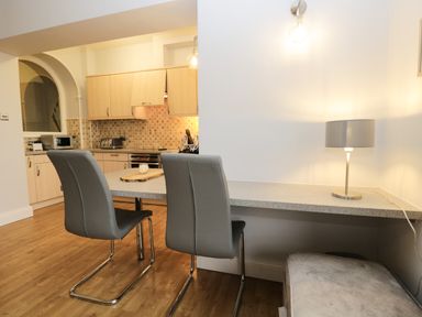 A kitchen with wooden floor gray chairs a countertop with a lamp and a microwave at Tethera in Bowness-On-Windermere