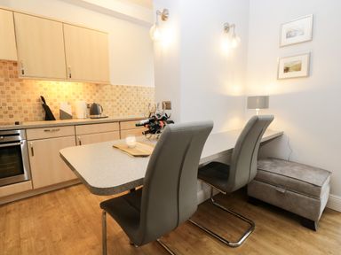 A kitchen with light wood cabinets two gray chairs and a countertop with a wine rack and candle at Tethera in Bowness-On-Windermere