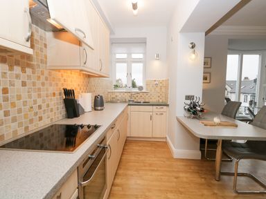 A kitchen with light wood cabinets electric stove and oven countertop extending to a dining area at Tethera in Bowness-On-Windermere