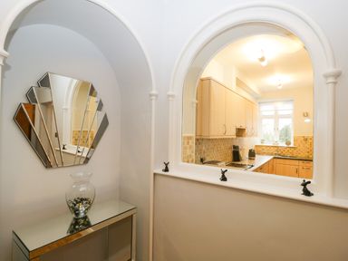 A kitchen seen through an arched pass through with a mirrored console table and decorative mirror in the foreground at Tethera in Bowness-On-Windermere