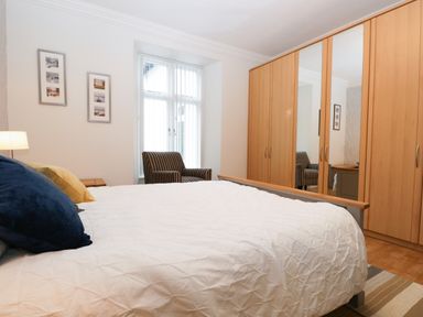 A bedroom with a bed a chair a window and a wardrobe with mirrored doors at Tethera in Bowness-On-Windermere