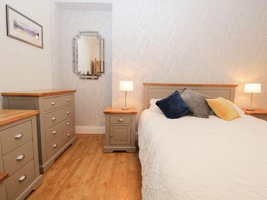 A bedroom with a bed with three pillows two lamps two bedside tables a chest of drawers a framed picture and a wall mirror at Tethera in Bowness-On-Windermere